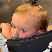 Maëna a rejoint le concours — aidez-le/la à gagner de superbes lots ! toddler, child, blue_eyes, pacifier, hair_bow, ponytail, stroller, indoor, wood_floor, furniture, close_up, face, cute, young_child, baby, head, people, portrait, infant, seat