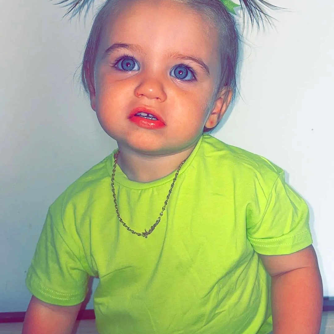 Maëna a rejoint le concours — aidez-le/la à gagner de superbes lots ! blue_eyes, casual_clothing, child, curious_expression, cute, face, floor, green_ribbons, indoor, isolated_background, necklace, neon_green_clothing, person, pigtails, portrait, short_sleeves, shorts, sitting, toddler, young_child