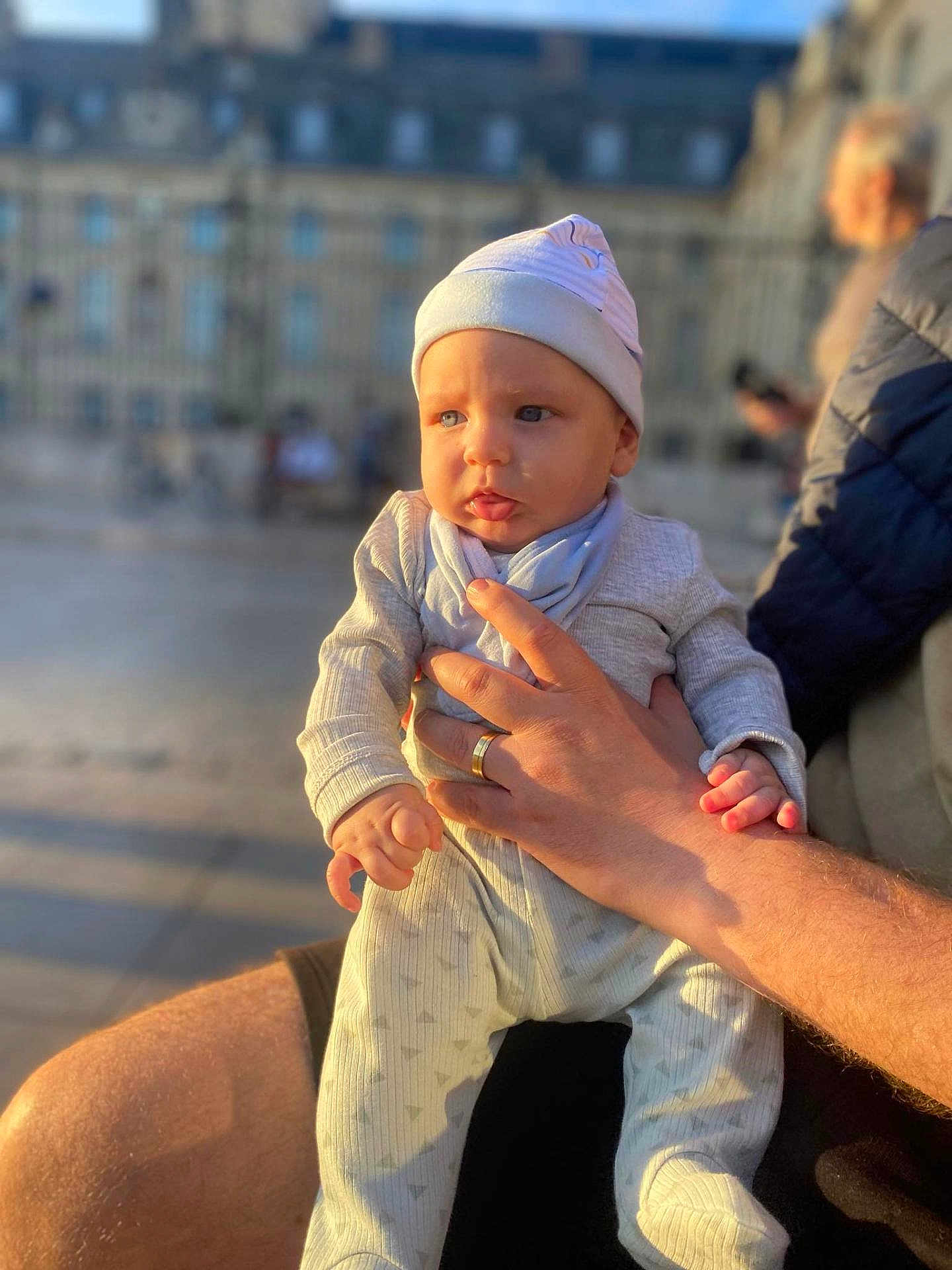 Bato a rejoint le concours — aidez-le/la à gagner de superbes lots ! baby, child, infant, person, human_hand, clothing, hat, adult_hand, outdoor, sunlight, portrait, holding, warm_light, blurred_background, face, expression, casual, daytime, people, urban