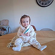 Noah participe au concours pour gagner de l'argent avec cette photo : baby, child, hoodie, hairbrush, table, blanket, socks, high_chair, clock, wooden_table, indoor, smiling, seated, curious, furniture, person, happy, home, cozy, casual
