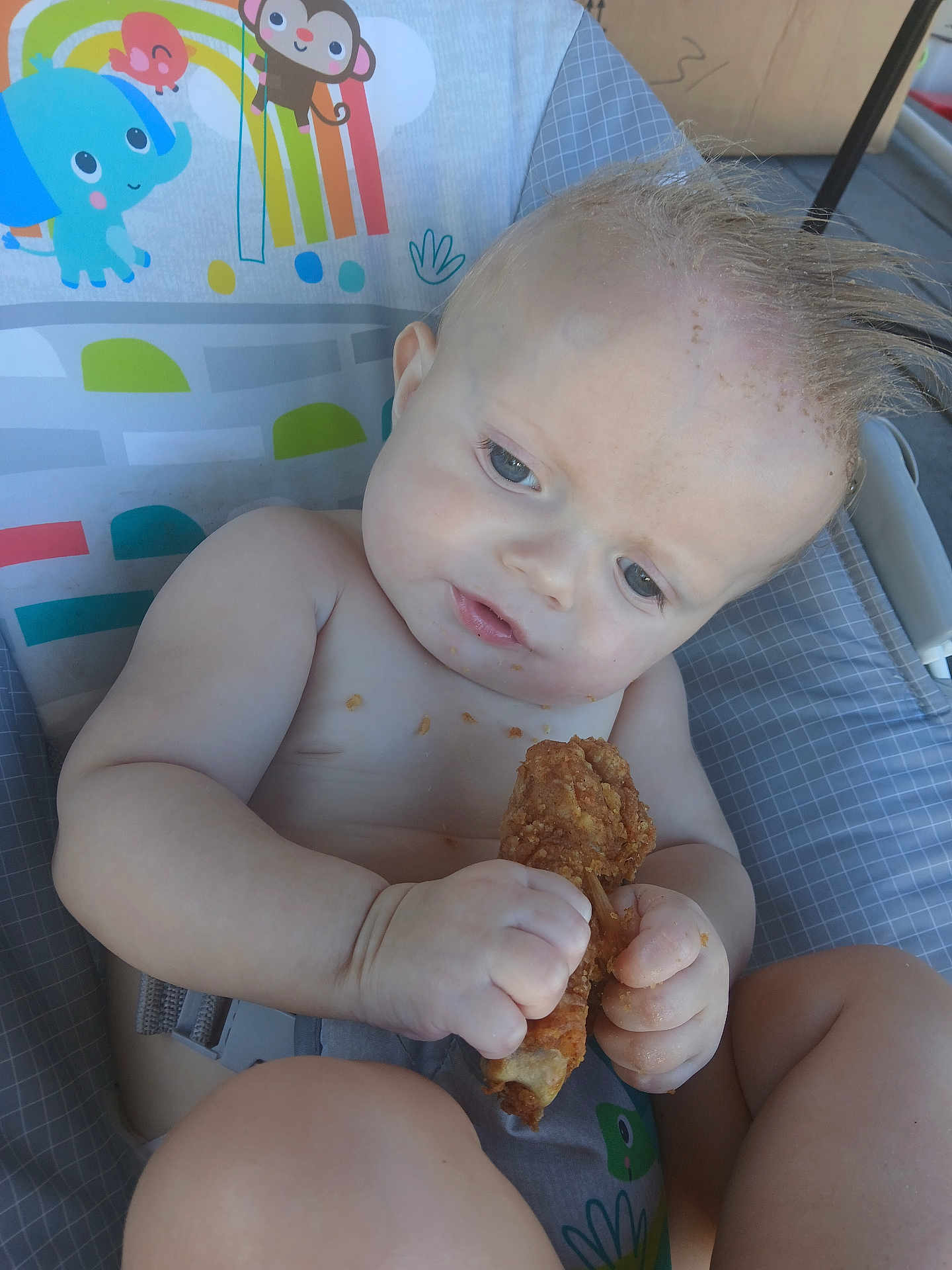 Remington is registered to the contest to win money with this photo: baby, child, fried_chicken, food, high_chair, mohawk, messy, crumbs, blue_eyes, indoor, seat_belt, clothing, colorful_background, table, hand, skin, face, cute, meal, curious