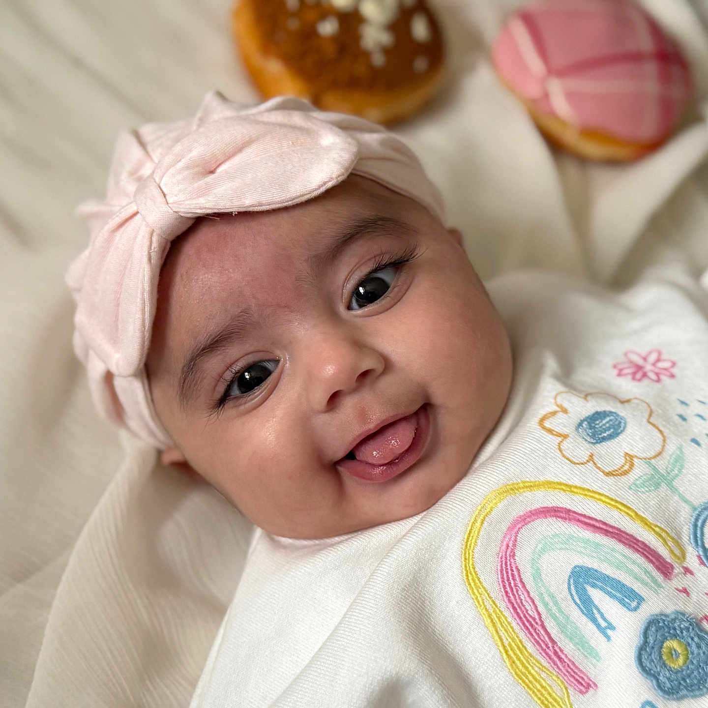 Zariah joined the competition — help win amazing prizes! baby, blanket, bow, closeup, clothing, cute, donut, face, flower, happy, headband, indoors, infant, lying_down, portrait, rainbow, smiling, soft_light, tongue, toy