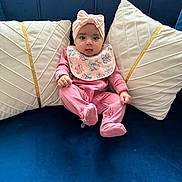 Zariah joined the competition — help win amazing prizes! baby, child, pink_clothing, headband, pillow, couch, blue_couch, indoor, infant, cute, smiling, seated, portrait, cozy, comfortable, baby_bib, decor, soft_furniture, person, home