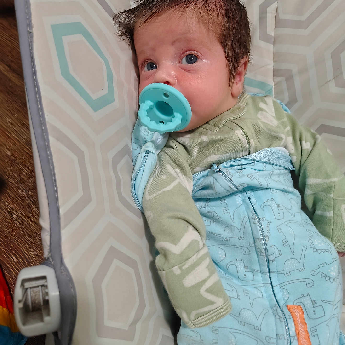 James is registered to the contest to win money with this photo: baby, pacifier, baby_rocker, onesie, dinosaur_print, infant, spiky_hair, blue_eyes, sleepwear, fabric_pattern, wood_floor, child, cute, lying_down, indoor, soft_lighting, portrait, comfort, baby_clothing, baby_accessory