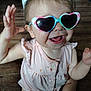 Aurora is registered to the contest to win money with this photo: baby, casual, child, cute, face, food_stains, hands_up, happy, heart_shaped, indoor, infant, messy, person, pink_clothing, playful, portrait, sitting, smiling, sunglasses, wooden_floor