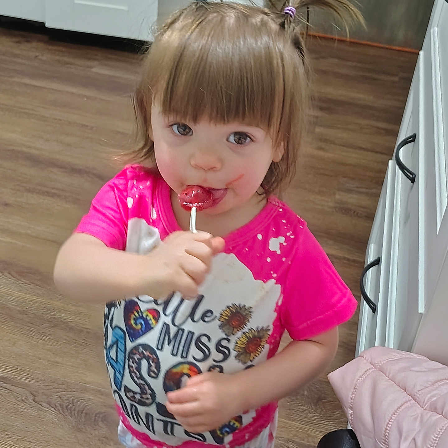 Aurora joined the competition — help win amazing prizes! toddler, child, lollipop, pink_shirt, pigtails, hair_ties, indoor, kitchen, wood_floor, cabinet, face, sweet, snack, messy_face, cute, young_child, person, smiling, playing, casual_clothing