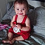 Aurora is registered to the contest to win money with this photo: baby, child, smiling, red_clothing, toy, bed, blanket, indoor, cute, happy, person, infant, hair_tie, sitting, holding, playful, young, portrait, face, room