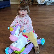 Aurora joined the competition — help win amazing prizes! toddler, child, toy, unicorn, ride_on_toy, indoor, floor, wooden_floor, pigtails, sweater, pants, boots, baby_gear, chair, room, curious, playful, colorful, plastic_toy, person