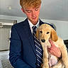 man, puppy, dog, golden_retriever, indoor, holding, suit, tie, young_adult, portrait, light, floor, carpet, door, hand, hair, face, casual, home, affection