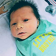 Jaxson is registered to the contest to win money with this photo: baby, newborn, infant, child, face, hair, clothing, pacifier, blanket, bed, lying_down, toddler, cute, sleepy, green_shirt, text_on_clothing, indoor, portrait, young_child, skin