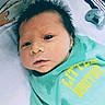 baby, newborn, infant, child, face, hair, clothing, pacifier, blanket, bed, lying_down, toddler, cute, sleepy, green_shirt, text_on_clothing, indoor, portrait, young_child, skin