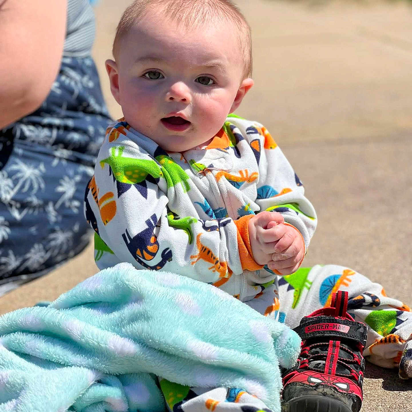 Georgie is registered to the contest to win money with this photo: baby, blanket, child, clothing, colorful, curious, cute, daylight, dinosaur_pajamas, hands, infant, outdoor, person, portrait, shoe, sidewalk, sitting, spiderman, sunny, young