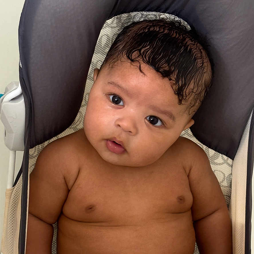 Karter joined the competition — help win amazing prizes! baby, infant, child, portrait, sitting, high_chair, curious, face, eyes, hair, dark_hair, smiling, skin, indoor, home, furniture, cushion, photography, closeup, shirtless
