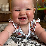 Aurora is registered to the contest to win money with this photo: baby, smiling, infant, face, arms, floor, rug, pattern, home_interior, wooden_furniture, basket, pillow, child, cute, happy, person, clothing, blond_hair, indoor, portrait
