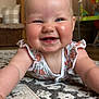 baby, smiling, infant, face, arms, floor, rug, pattern, home_interior, wooden_furniture, basket, pillow, child, cute, happy, person, clothing, blond_hair, indoor, portrait