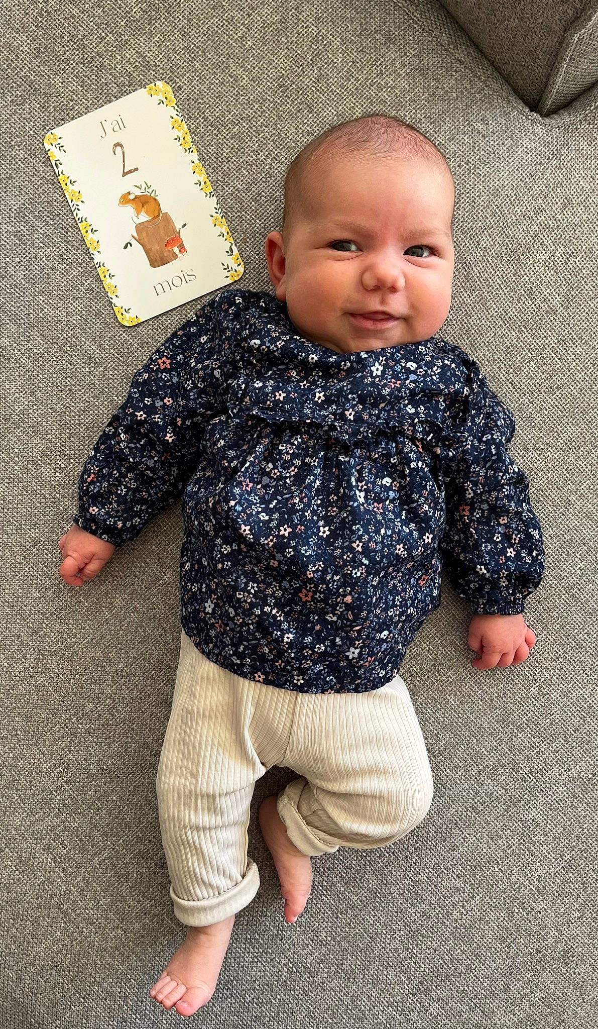 Nina participe au concours pour gagner de l'argent avec cette photo : arm, baby, baby_toddler_clothing, cheek, child, floor, flooring, fun, head, human_leg, joint, leg, nose, outerwear, pattern, person, sitting, sleeve, t_shirt, toddler