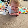 Joshua joined the competition — help win amazing prizes! baby, tummy_time, play_mat, onesie, smiling, indoor, carpet, toy, child, living_room, couch, blanket, floor, person, cute, happy, infant, play, head, expression