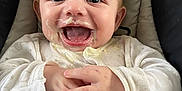 Joshua is registered to the contest to win money with this photo: baby, child, messy, food, laughing, happy, white_clothing, cushion, seat, hands, face, mouth_open, eyes, infant, cute, portrait, indoors, closeup, smiling, joyful