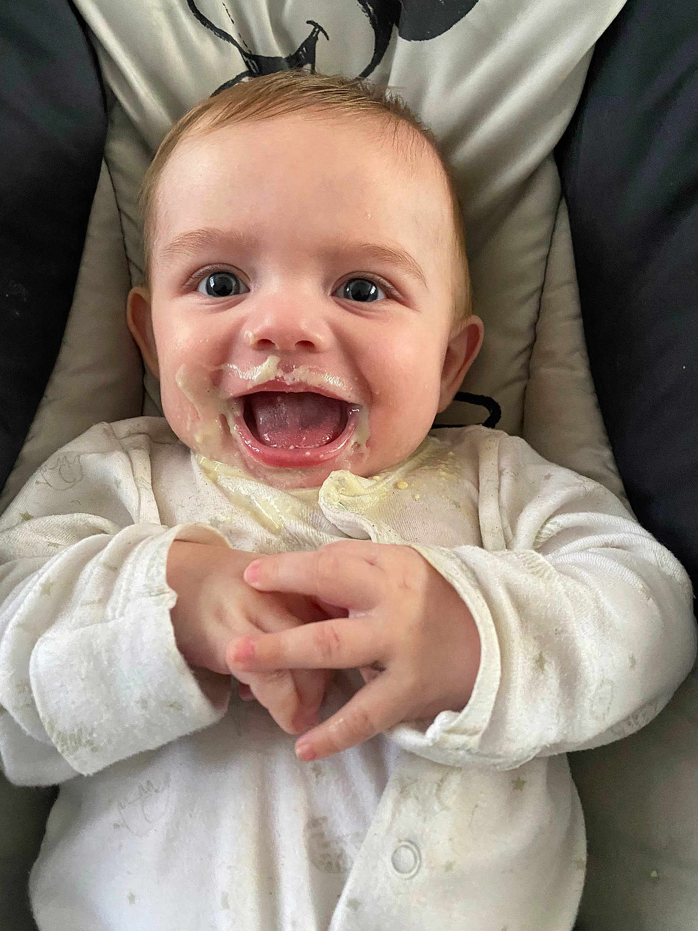 Joshua is registered to the contest to win money with this photo: baby, child, messy, food, laughing, happy, white_clothing, cushion, seat, hands, face, mouth_open, eyes, infant, cute, portrait, indoors, closeup, smiling, joyful
