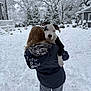 snow, dog, puppy, person, winter, snowy_backyard, trees, snow_on_clothing, house, outdoor, cold_weather, black_and_white_dog, holding, fur, nature, back_view, frozen, snowfall, playful, cuddling