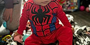 Rowan joined the competition — help win amazing prizes! baby, blanket, blurred_background, child, costume, cute, expression, face, floor, footed_pajamas, hat, indoor, pattern, person, playtime, red_clothing, sitting, spiderman, toy, young_child