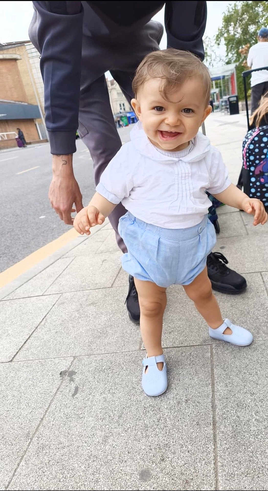 Rowan is registered to the contest to win money with this photo: toddler, child, smiling, walking, sidewalk, urban, adult, hand, white_shirt, blue_shorts, baby_shoes, outdoor, daylight, person, street, happiness, cute, support, city, casual_clothing