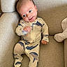 baby, infant, onesie, whale_pattern, couch, beige, smile, face, hand, furniture, indoor, cute, child, relaxed, seated, portrait, home, cozy, expression, person
