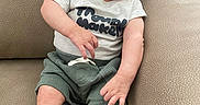 James is registered to the contest to win money with this photo: baby, smiling, sitting, shirt, shorts, couch, furniture, happy, infant, person, skin, foot, hand, face, head, indoors, cute, relaxed, comfort, young_child