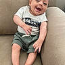 baby, smiling, sitting, shirt, shorts, couch, furniture, happy, infant, person, skin, foot, hand, face, head, indoors, cute, relaxed, comfort, young_child