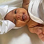 baby, infant, white_bow, tongue_out, blanket, cute, smiling, closeup, face, headwear, soft_texture, newborn, lying_down, skin, adorable, child, cute_expression, indoors, warm_light, playful