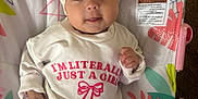Aireigh is registered to the contest to win money with this photo: baby, infant, girl, headband, bow, onesie, text, clothing, baby_seat, floral_pattern, colorful, smiling, cute, lying_down, face, hand, foot, indoors, soft_toys, warning_label