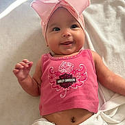 Aireigh is registered to the contest to win money with this photo: baby, child, pink_bow, headband, tank_top, harley_davidson, smile, lying_down, blanket, cute, infant, skin, face, arm, hand, belly_button, white_blanket, indoors, soft_light, happy