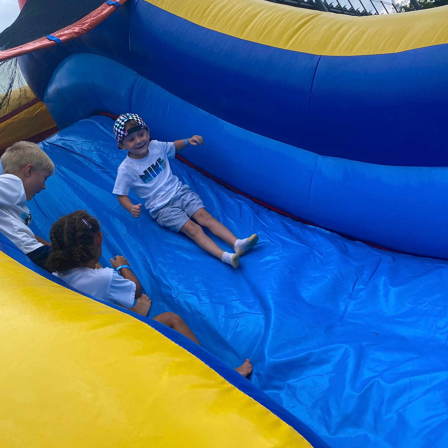 Solan Blayne is registered to the contest to win money with this photo: activity, blue, boy, cap, children, cloudy_sky, friends, fun, group, happy, inflatable_slide, outdoor, play, recreation, shorts, smile, socks, summer, tshirt, yellow