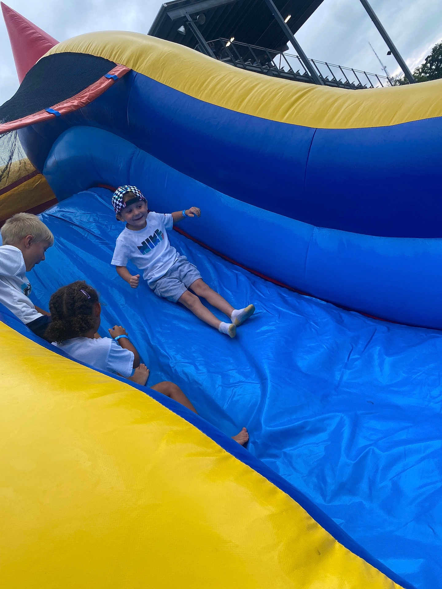Solan Blayne is registered to the contest to win money with this photo: children, inflatable_slide, outdoor, play, fun, boy, cap, tshirt, shorts, socks, smile, happy, summer, activity, recreation, group, friends, blue, yellow, cloudy_sky