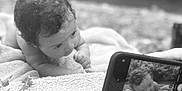 Beretta is registered to the contest to win money with this photo: baby, infant, blanket, curly_hair, smartphone, photo, portrait, black_and_white, hand, texture, face, lying_down, closeup, outdoor, nature, leaf, reflection, camera, cute, expression
