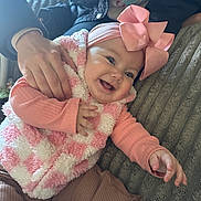 Braelynn is registered to the contest to win money with this photo: baby, child, smiling, pink_bow, pink_vest, hand, adult_hand, blanket, cozy, happy, infant, cute, portrait, indoor, clothing, headwear, baby_girl, toddler, warm_lighting, texture