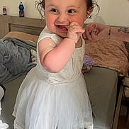Amélia participe au concours pour gagner de l'argent avec cette photo : toddler, child, white_dress, bed, smiling, happy, indoor, hand, blanket, pillow, person, cute, playful, hair_bow, skin, foot, furniture, portrait, baby, room