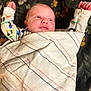 arms_up, baby, blanket, blue_eyes, clothing, cozy, curious, cute, face, floral_pattern, human, indoors, infant, lying_down, newborn, peaceful, portrait, small_hands, soft_texture, striped