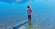 Scarlett is registered to the contest to win money with this photo: barefoot, blue_sky, child, clear_water, exploration, grass, nature, outdoor, pants, peaceful, reflection, ripples, rocks, shallow_water, shirt, standing, sunlight, tie_dye, water, young
