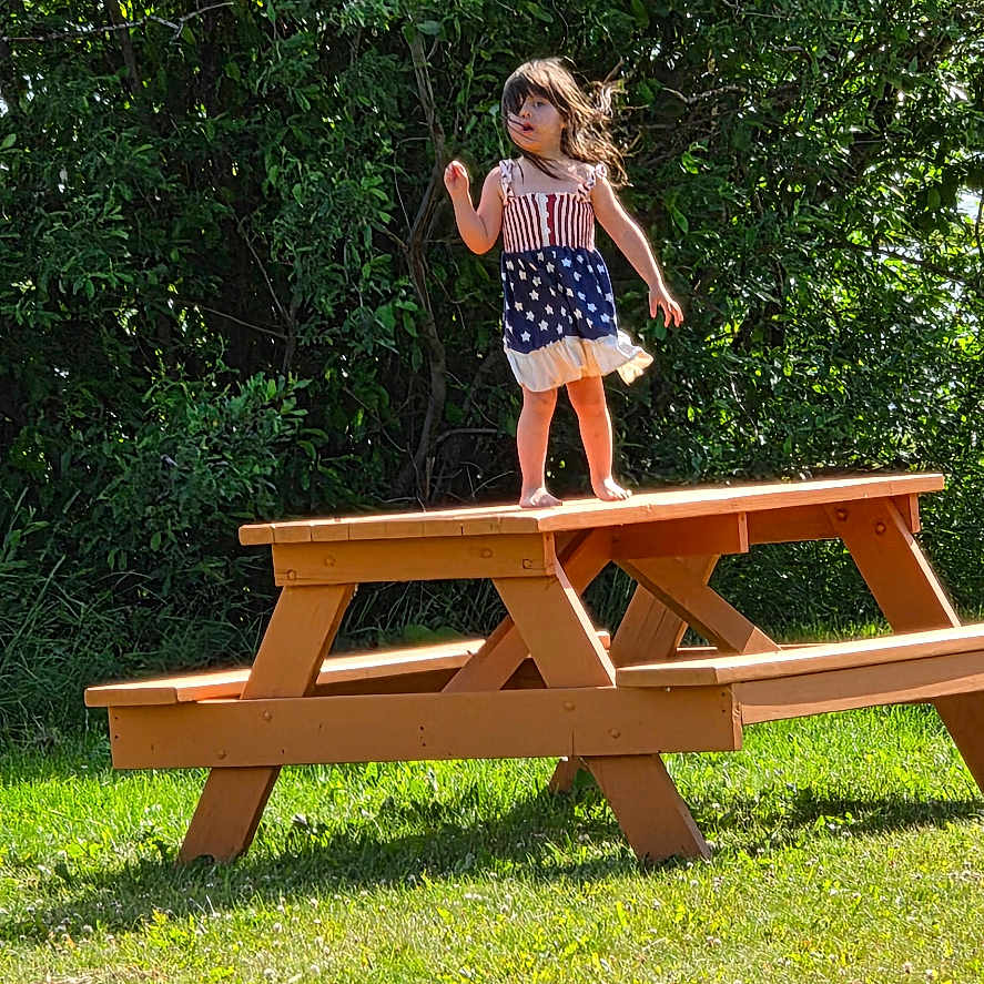 Sofie is registered to the contest to win money with this photo: casual, child, daytime, dress, fun, girl, grass, greenery, happy, nature, outdoor, park, picnic_table, play, standing, summer, sunlight, trees, wood, youth