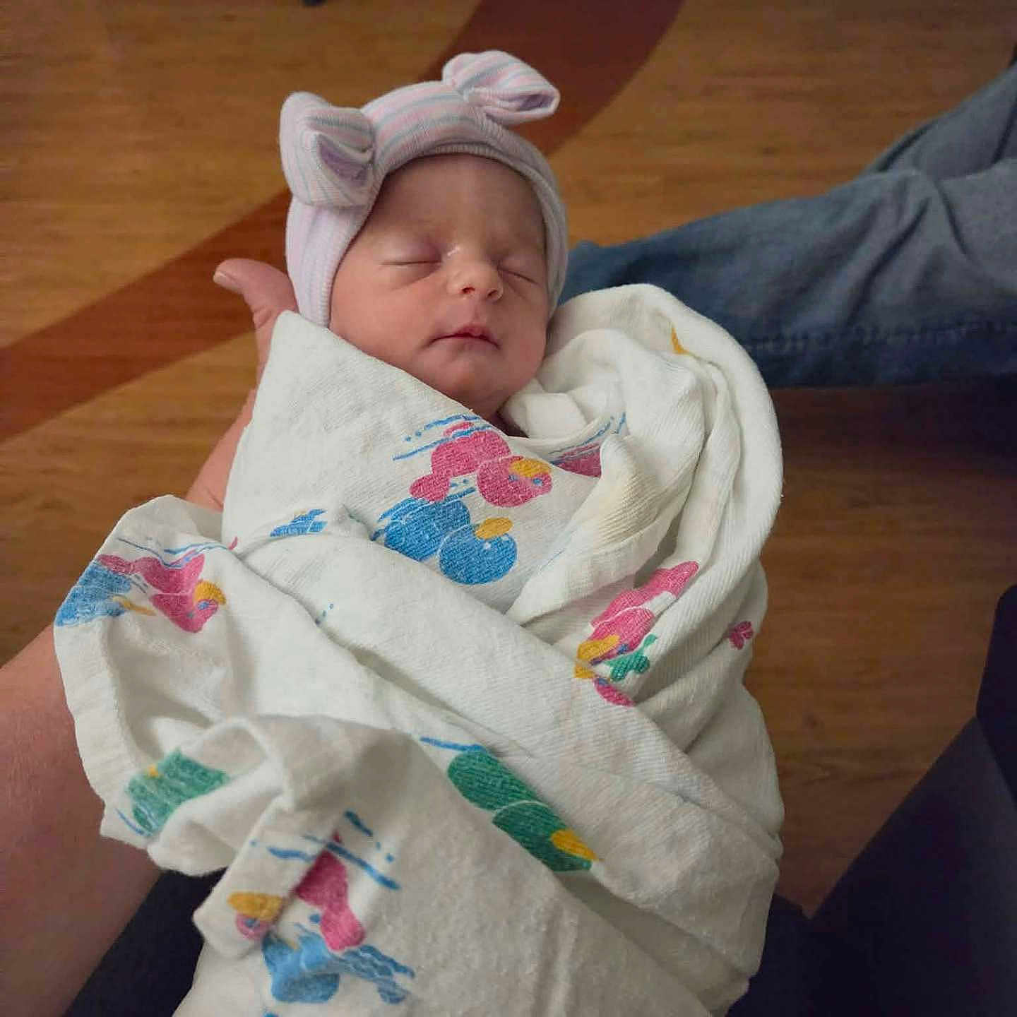Aria is registered to the contest to win money with this photo: newborn, baby, infant, wrapped, blanket, hat, bunny_ears, sleeping, hand, wooden_floor, hospital, person, indoor, cute, peaceful, soft, portrait, clothing, resting, human