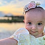 baby, child, portrait, face, flower_headband, yellow_dress, cute, smiling, outdoor, sunset, nature, water, sky, blurry_background, happy, infant, person, closeup, arm, headwear