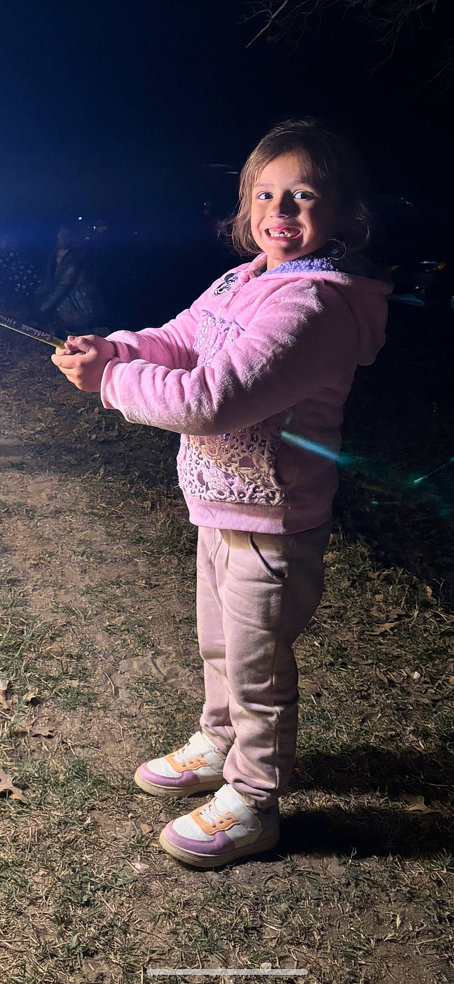 Holland joined the competition — help win amazing prizes! casual_clothing, celebration, child, dark_background, face, fun, grass, happy, holding, joy, night, outdoor, pants, person, pink_hoodie, smiling, sneakers, sparkler, standing, toy