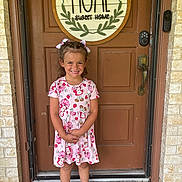 Holland is registered to the contest to win money with this photo: barefoot, brick_wall, child, concrete, curly_hair, daylight, door, dress, footwear, front_door, girl, hair_bows, happy, home_sign, outdoor, person, plaid_bow, smiling, standing, welcome_mat