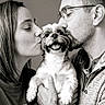 affection, black_and_white, casual_clothing, close_up, cute, dog, face, friendly, glasses, happy, holding, indoor, kiss, love, man, people, pet, portrait, smile, woman