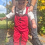 toddler, child, boy, outdoor, sunlight, red_clothing, vest, pants, white_shoes, cap, bow_tie, person, adult_hands, supporting, walking, sidewalk, shoes, nature, plants, happy