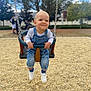 baby_swing, casual_clothing, chain, child, daylight, denim_overalls, fun, gravel_ground, happy, holding, necklace, outdoor, park, people_in_background, person, playground, smile, toddler, tree, white_sneakers