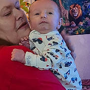 Lucas is registered to the contest to win money with this photo: baby, adult, holding, onesie, vehicle_pattern, red_shirt, face, portrait, indoor, poster, jungle_theme, lion, giraffe, colorful, person, child, hand, clothing, wall, closeup