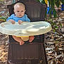 Lucas is registered to the contest to win money with this photo: baby, child, high_chair, wooden_chair, outdoor, leaves, tree_branches, baby_clothing, blue_sweater, feet, hands, nature, sunlight, portrait, infant, seat, person, face, expression, background_blur