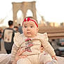 Maya is registered to the contest to win money with this photo: baby, child, infant, headband, red, clothing, minnie_mouse, sitting, hands, outdoor, bridge, people, cityscape, portrait, cute, wide_eyes, sock, casual_wear, daytime, person